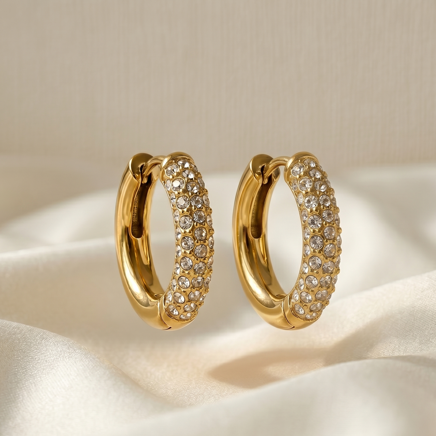 Gold hoop earrings with clear stones on a beige fabric background