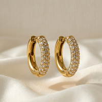 Gold hoop earrings with clear stones on a beige fabric background