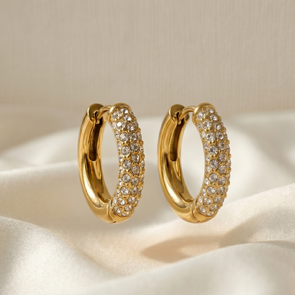 Gold hoop earrings with clear stones on a beige fabric background