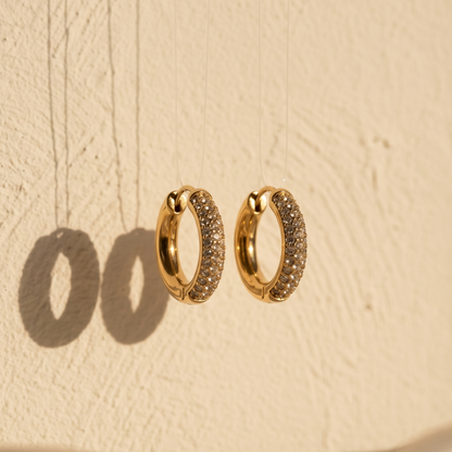 Gold hoop earrings with embedded stones on a beige textured background