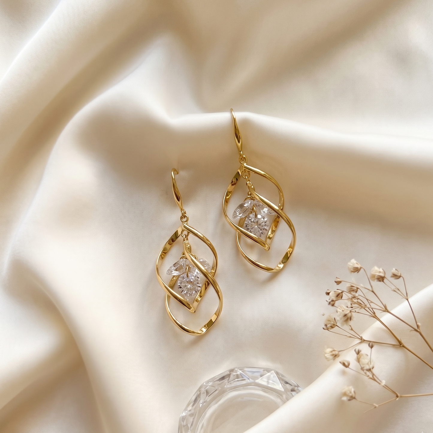 Gold earrings with clear stones on a beige fabric background