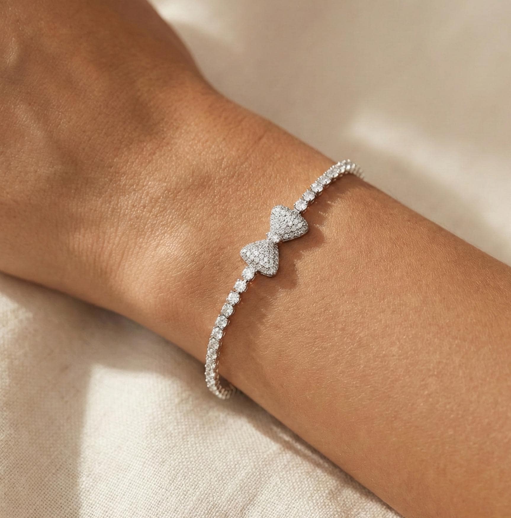 White gold crystal bow bracelet with pavé bow centerpiece and tennis style crystal chain. Elegant feminine bracelet featuring sparkling crystals and white gold filled finish. Lightweight and comfortable jewelry designed for everyday wear or special occasions. Beautiful gift bracelet perfect for Valentine’s Day, anniversaries, birthdays, bridesmaids, or romantic gifts for women.
