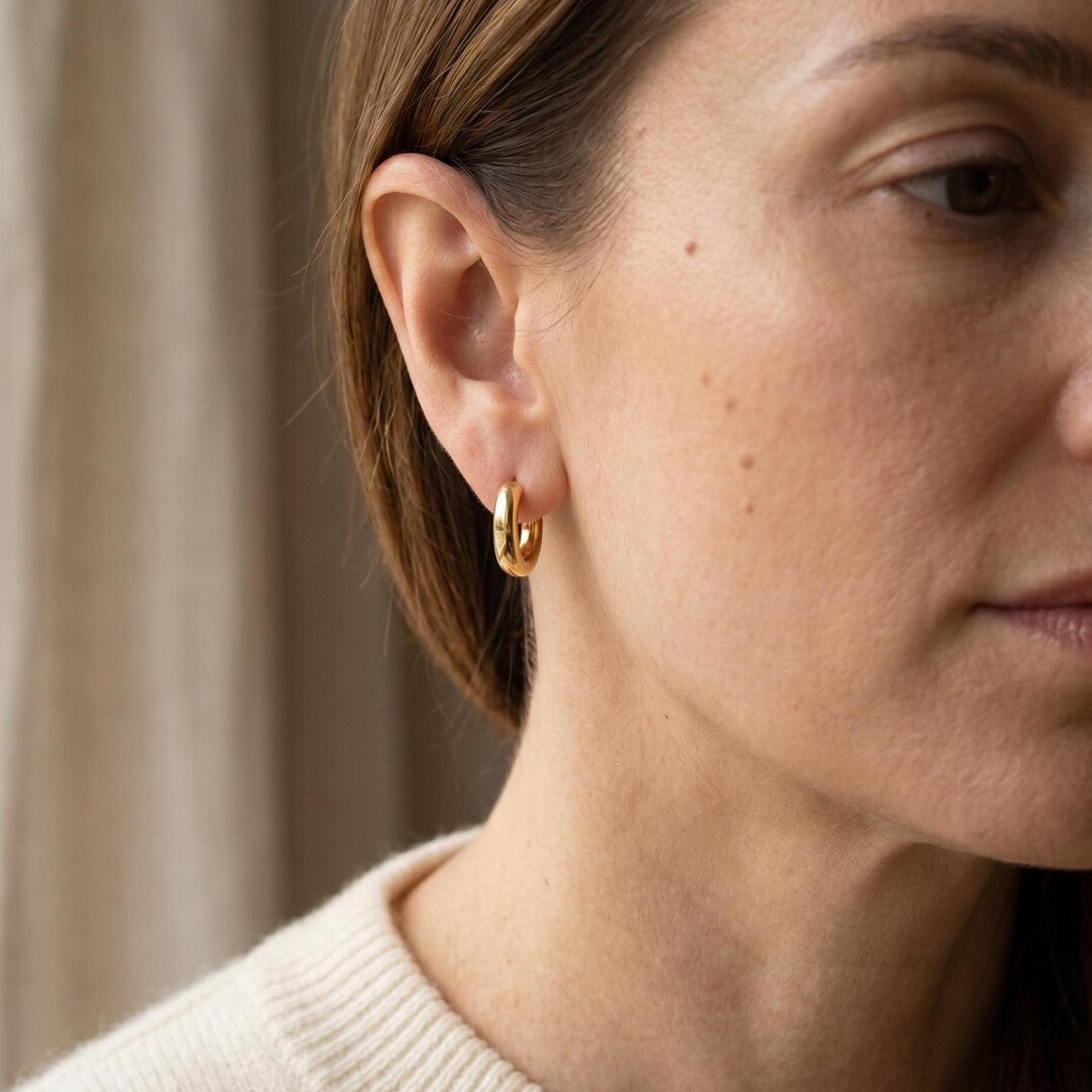 Gold oval huggie hoops worn on earlobe close-up