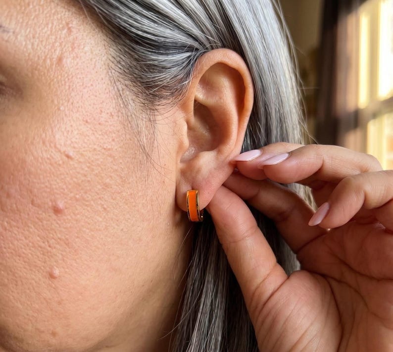Model wearing orange enamel huggie hoop earring
