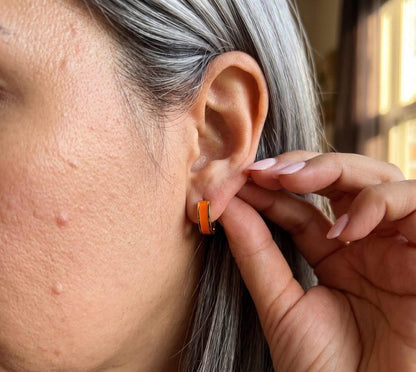 Model wearing orange enamel huggie hoop earring