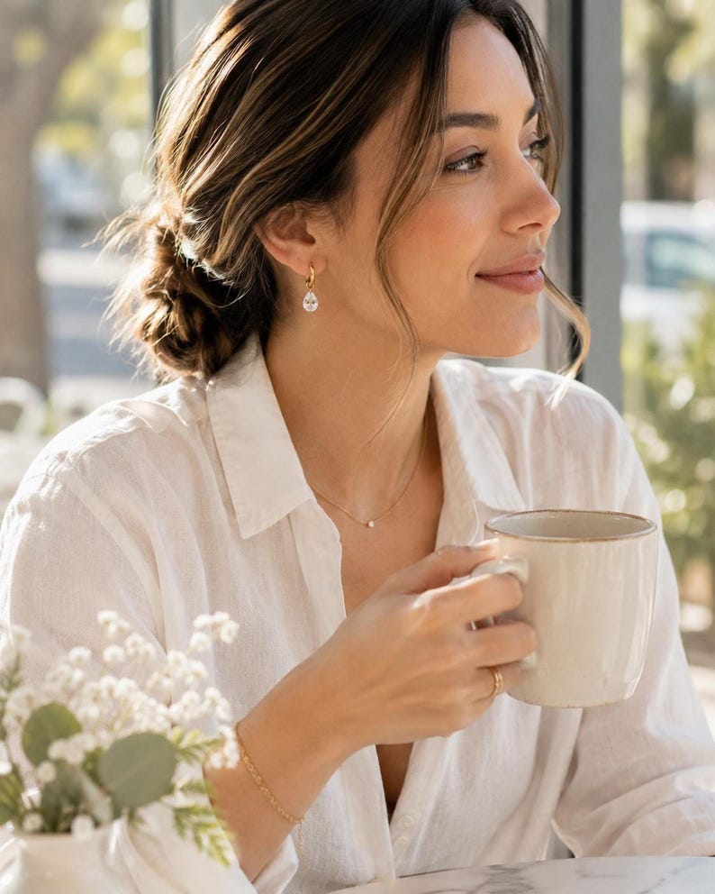 Model wearing gold huggie earring with CZ teardrop, holding mug