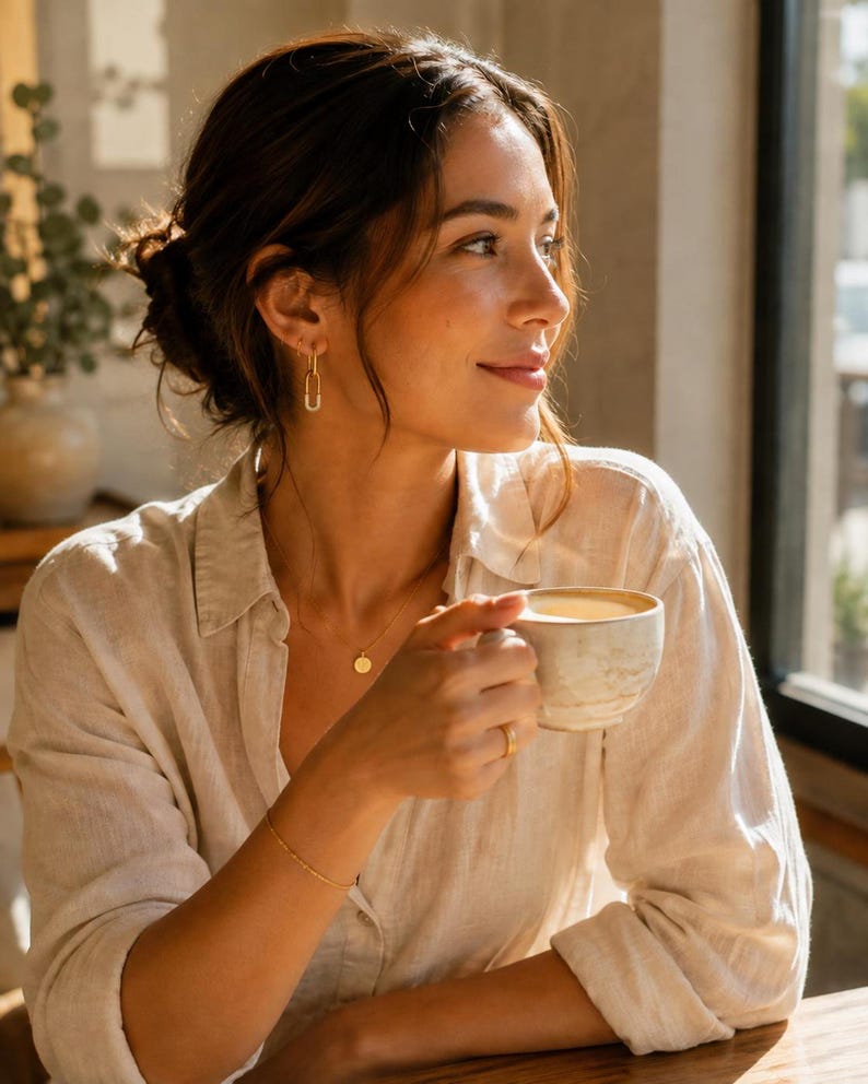 Model wearing gold safety pin huggie hoop earring with coffee