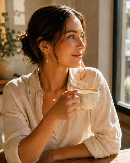 Model wearing gold safety pin huggie hoop earring with coffee