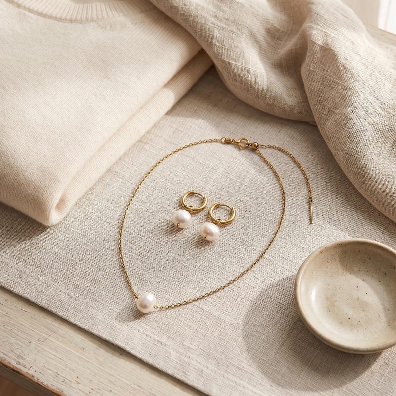 Pearl necklace and earrings set flat lay with sweater