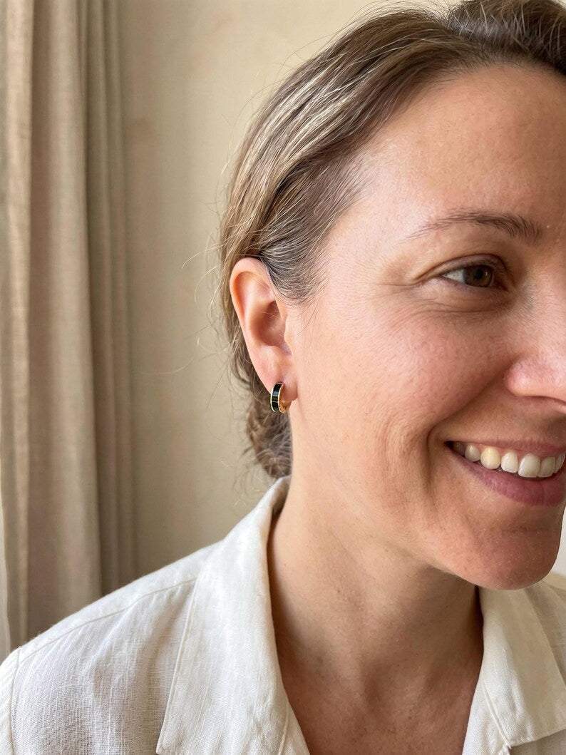Model smiling wearing black enamel huggie hoop earring