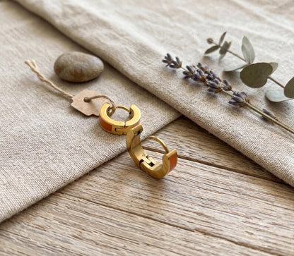 Orange enamel huggie hoop earrings on linen with lavender