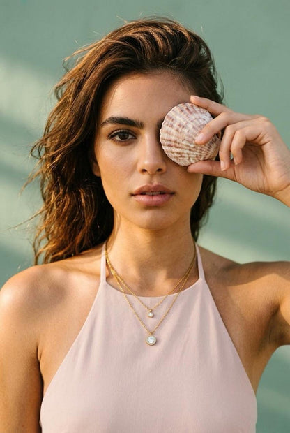 Model wearing layered gold CZ necklace with seashell