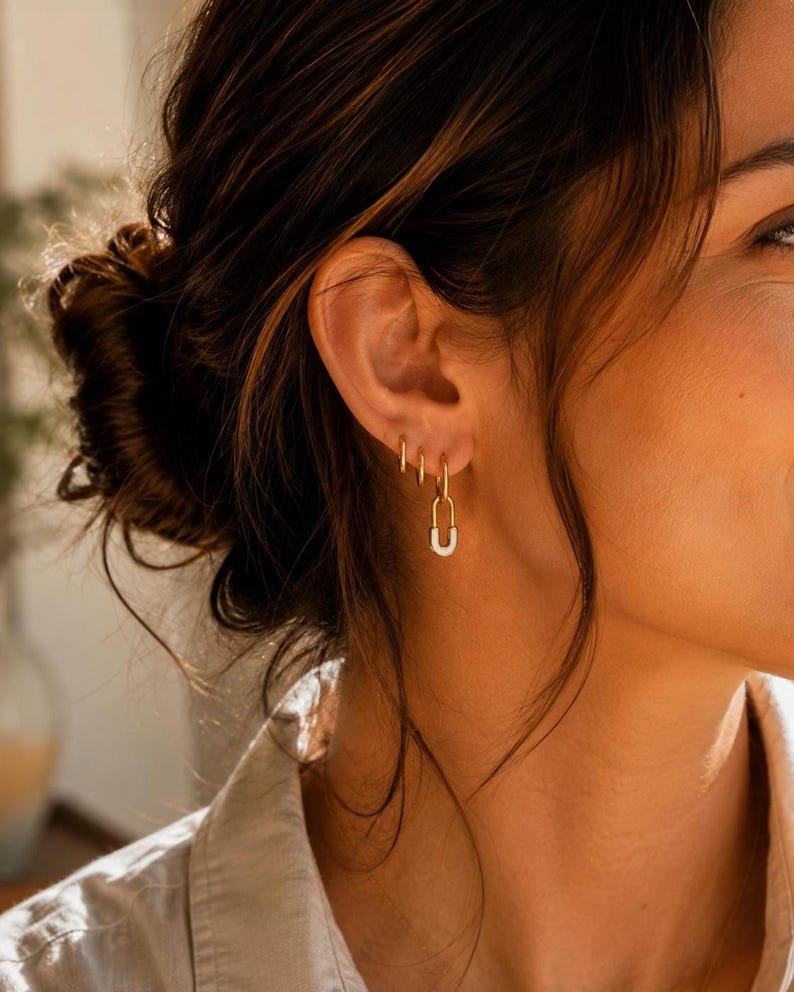 Back view of ear wearing gold safety pin huggie hoop earring