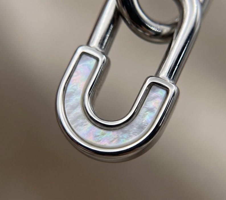 Close up of silver safety pin huggie hoop earring mother of pearl inlay