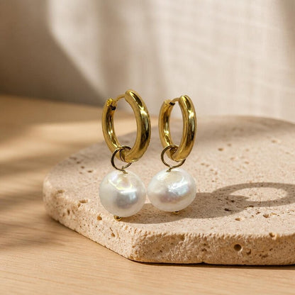 Gold huggie hoop earrings with dangling pearls on stone slab
