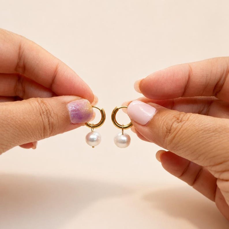 Hands holding gold huggie earrings with dangling pearls