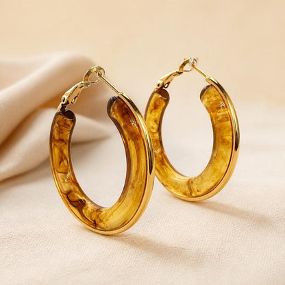 Gold-trimmed tortoiseshell resin hoop earrings on textured fabric