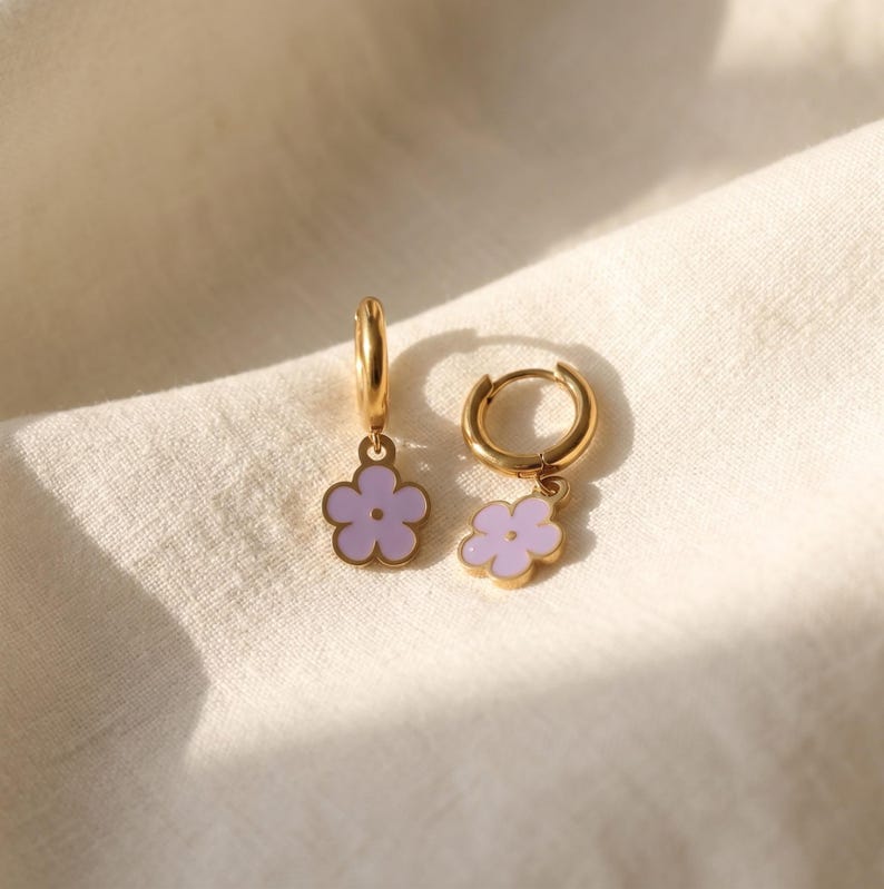 Pair of gold huggie hoop earrings with purple enamel flower charms