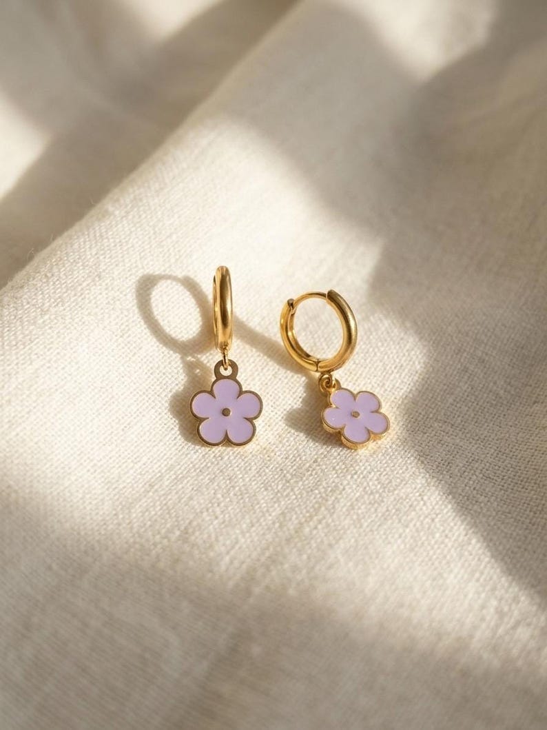 Gold hoop earrings with lilac flower charms on fabric