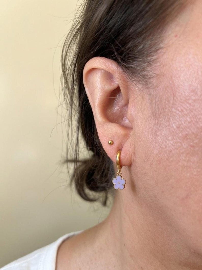 Close-up of ear wearing gold hoop with purple flower pendant