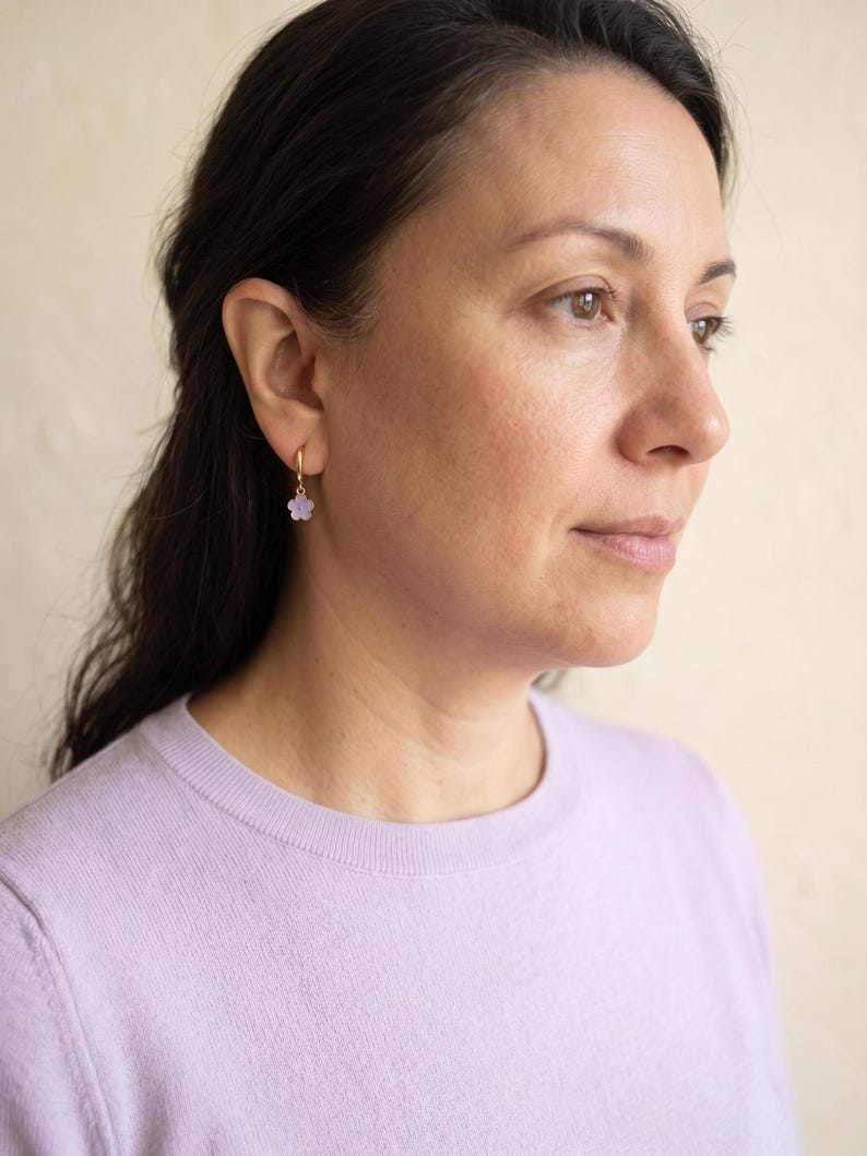 Person wearing gold flower huggie earring and lilac sweater