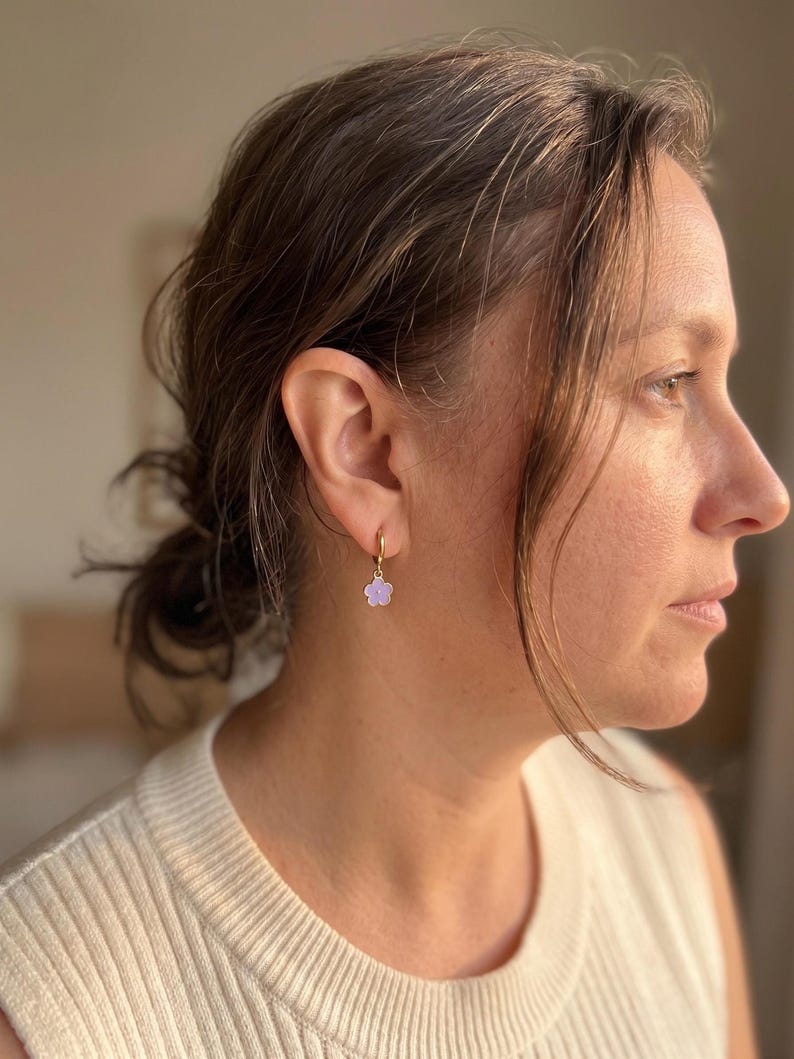 Side view of person wearing gold hoop with purple flower pendant