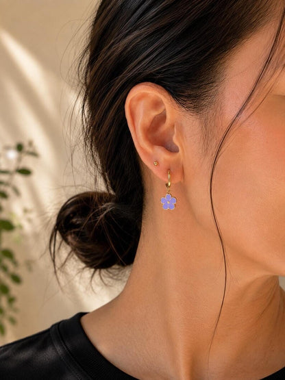 Close-up of ear wearing gold hoop and purple enamel flower dangle