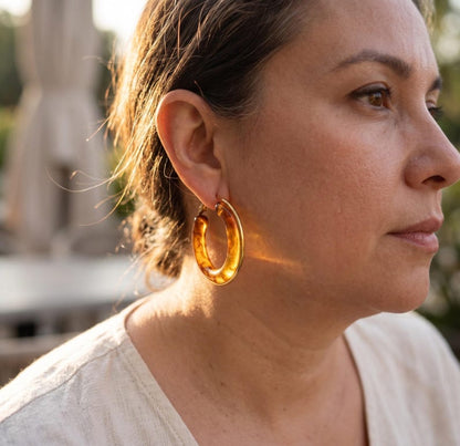 Profile view of amber resin hoop earring outdoors in sunlight