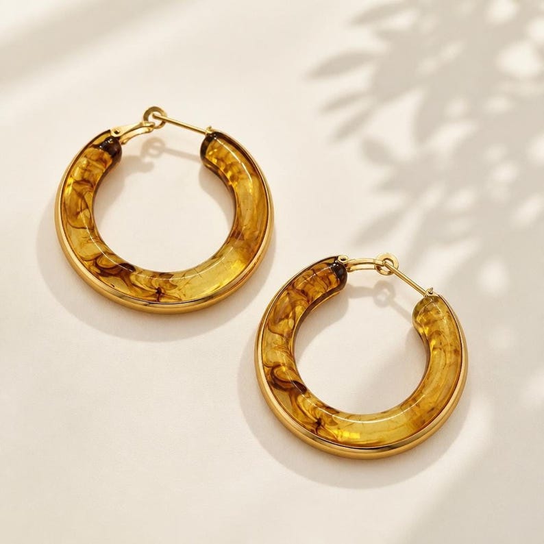 Tortoiseshell resin hoop earrings with gold edges on flat surface