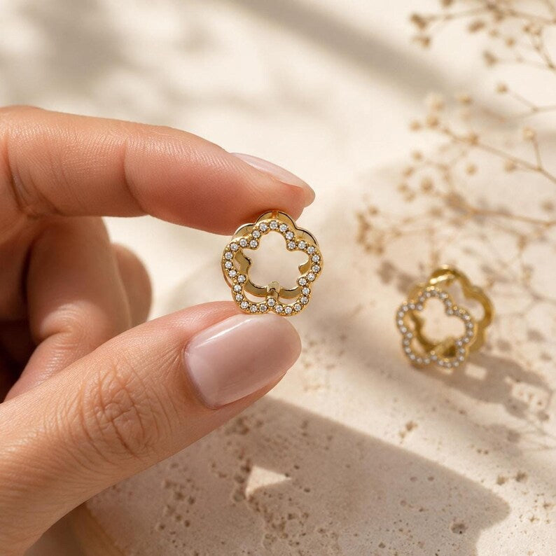 Hand holding gold floral huggie earring with clear stones