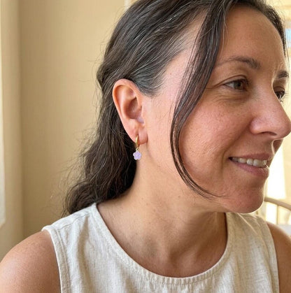 Profile view of woman wearing gold huggie earring with purple flower charm