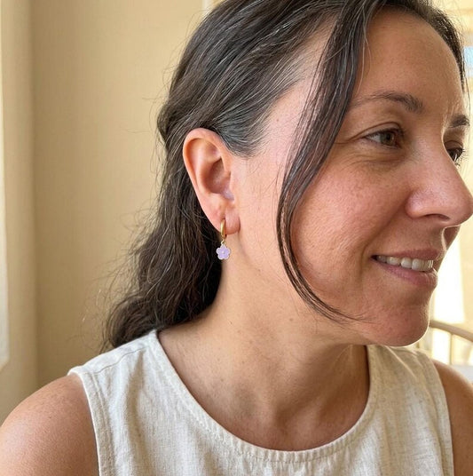 Profile view of woman wearing gold huggie earring with purple flower charm