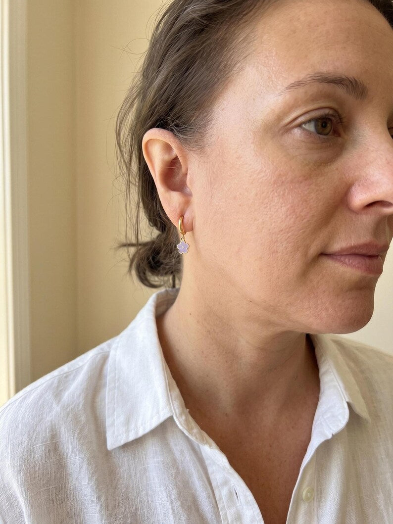 Person wearing gold huggie earring with purple enamel flower charm