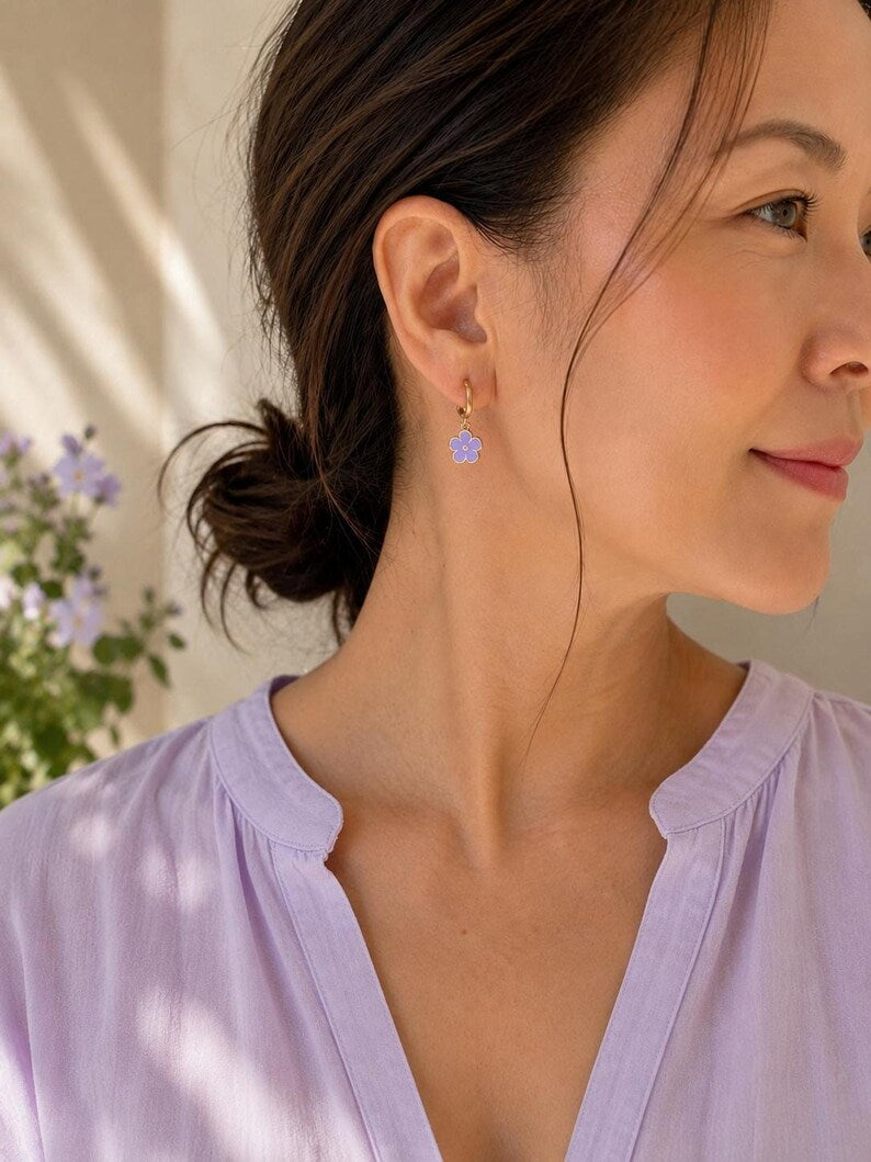 Person wearing gold flower charm huggie earring and lavender top