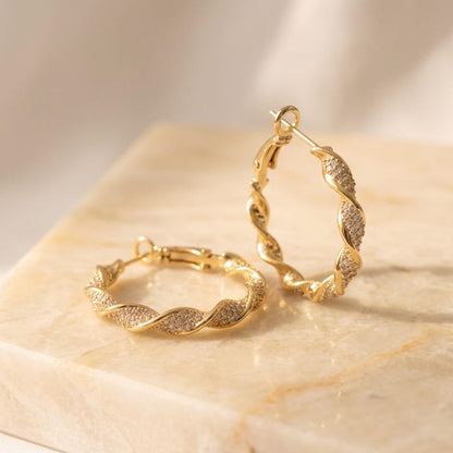Gold twisted crystal pave hoop earrings on surface