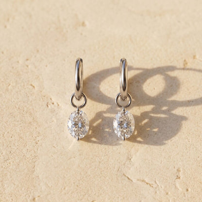 Moissanite huggie earrings lying flat on textured surface