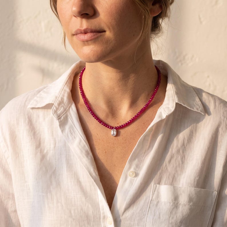Person wearing ruby bead necklace with white collared shirt