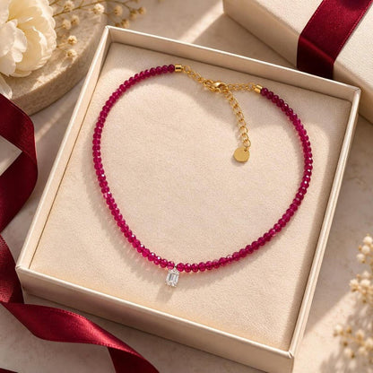 Ruby beaded necklace coiled in open gift box with red ribbon