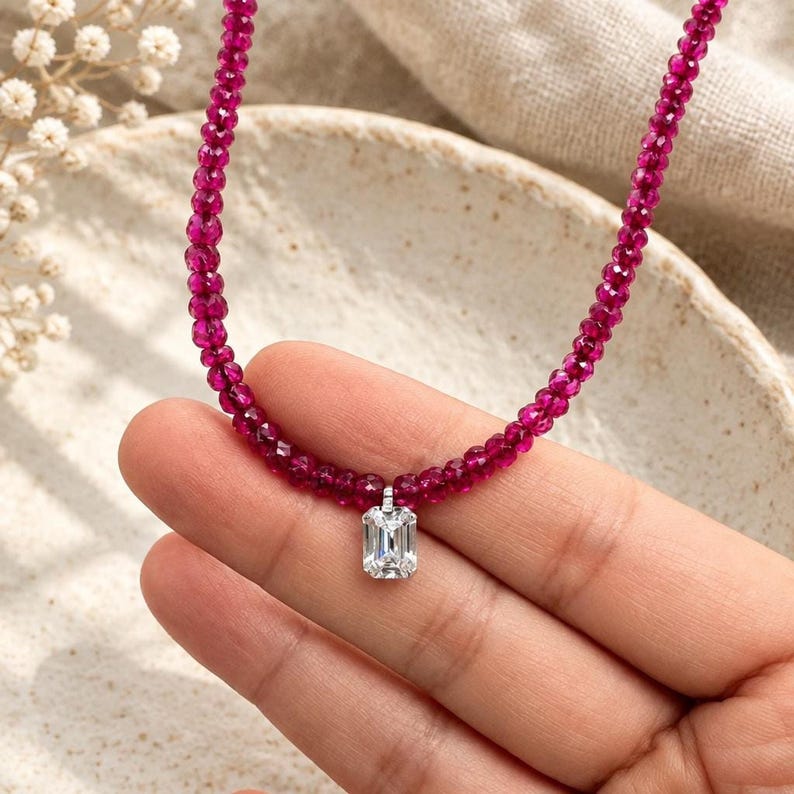 Hand holding emerald-cut pendant and ruby bead strand