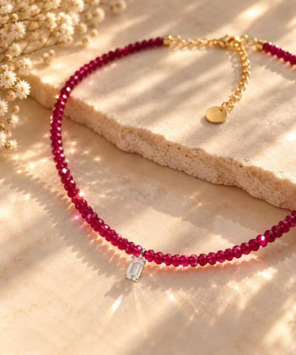 Ruby beaded necklace on textured stone surface with dried flowers